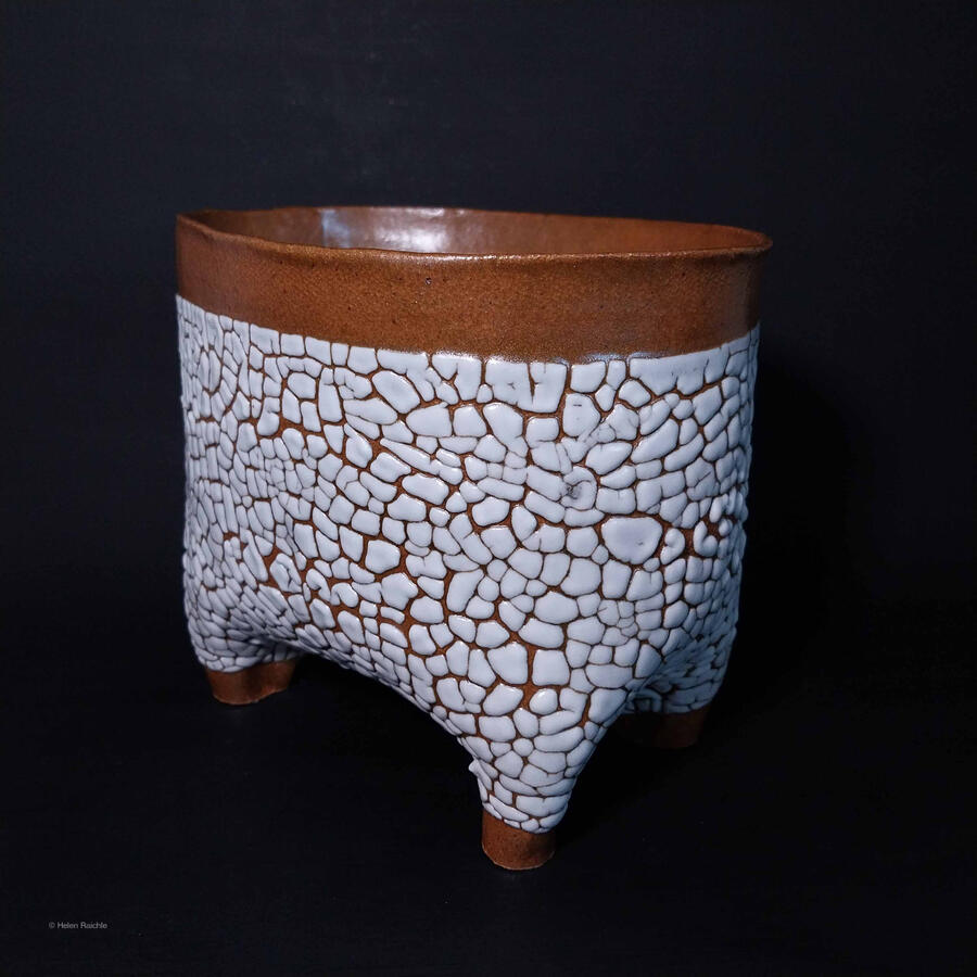 An oblong flower pot with four hollow legs for drainage. The pot has an orange-gold rim and feet with a white, crackle textured glaze body. Interior is not glazed.