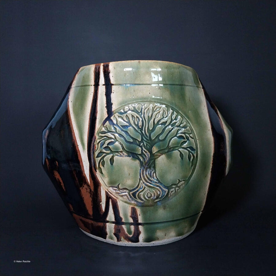 A green, octagonal stoneware vase with a tree in a circle impressed into the center. The sides/corners of the vase are glazed black-brown.