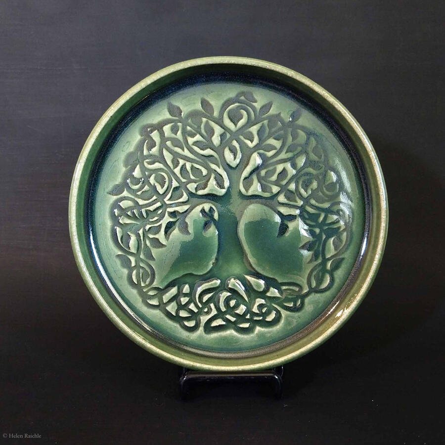Round dark green stoneware plate with Celtic knot style tree impressed in center. The canopy and trunk extend to the edges of the plate