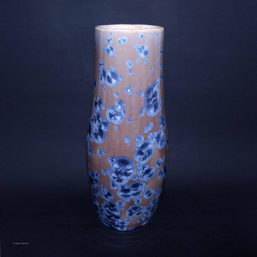 A tall, narrow, bottle shaped stoneware vase with blue crystalline glaze. The blue crystals are round and mostly clustered. Some appear as though they are dividing as in cell mitosis. The crystals are chatoyant. The interior is glazed light yellow.