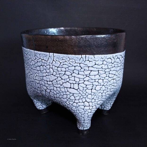 An oblong flower stoneware pot with four hollow legs for drainage. The pot has a black rim and black feet with a white, crackle textured glaze body. Interior is not glazed.