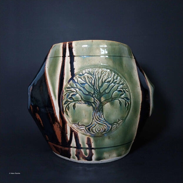 A green, octagonal stoneware vase with a tree in a circle impressed into the center. The sides/corners of the vase are glazed black-brown.