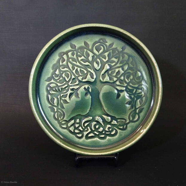 Round dark green stoneware plate with Celtic knot style tree impressed in center. The canopy and trunk extend to the edges of the plate