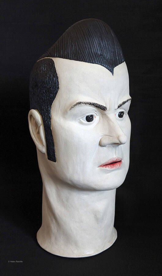 A bust of a man includes his head and neck. His black hair is styled high in a pompadour. His brows are furrowed and his red lips are slightly parted.